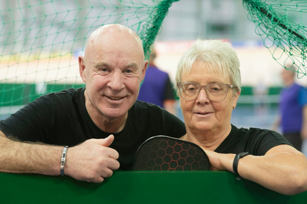 Smiling couple holding pickleball paddles at the court